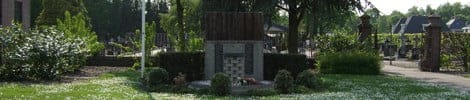 A monument in a leafy cemetery surrounded by trees