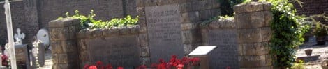 Gedenkmauer aus Stein mit Inschriften und roten Blumen